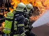 Zwei Feuerwehrmänner halten einen Wasserschlauch, um ein Feuer zu löschen