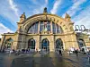 Frankfurter Bahnhofsgebäude von vorne, Passanten davor, blauer Himmel, einige weiße Wolken