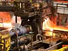 Hot steel being rolled to shape in mill in steel manufacturing plant.