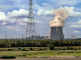 Antwerpen, Flanders, Belgium - July 10, 2022: Sunset on Cooling towers and Doel Nuclear Power plant under blue cloudscape with green nature reserve up front. Tall electricity pylons