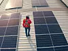 Mann kontrolliert auf einem Industriehallendach eine PV-Anlage
