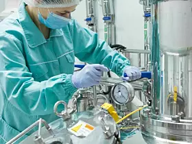 Pharmaceutical factory woman worker in protective clothing operating production line in sterile environment