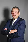 Mann im blauen Anzug mit roter Brille vor grauem Hintergrund, Arme verschränkt. Andreas Ritter, Strategic Account Director bei ivoflow